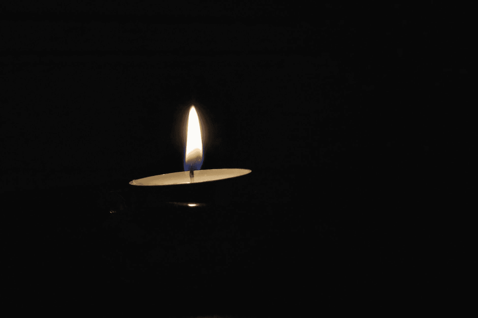 Single candle flame glowing warmly in soft darkness representing hope and gentle resilience