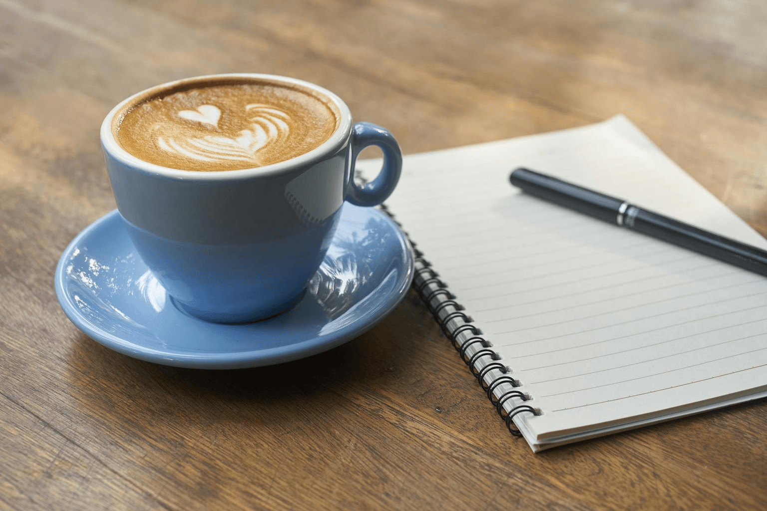 Open journal with a glowing pen beside morning coffee in warm golden light representing deep reflective journaling