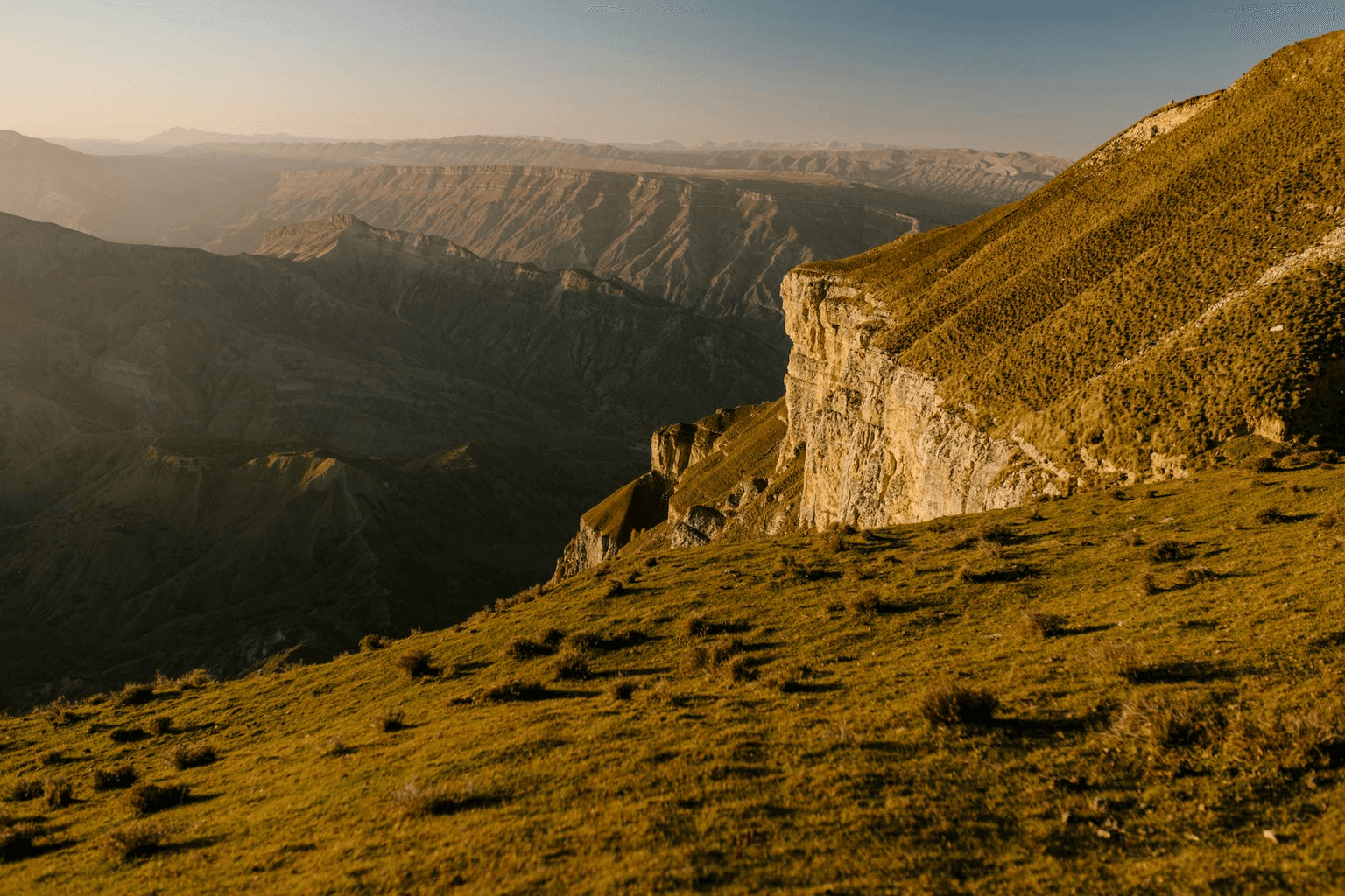 Person standing at the edge of a stunning mountain vista at golden hour with arms open representing travel freedom and dream destinations