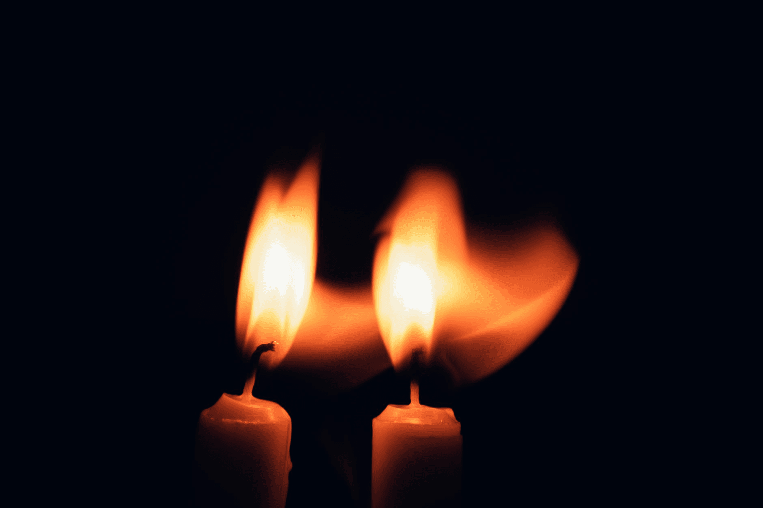 Two flames merging into one golden light against a dark background, representing twin flame union