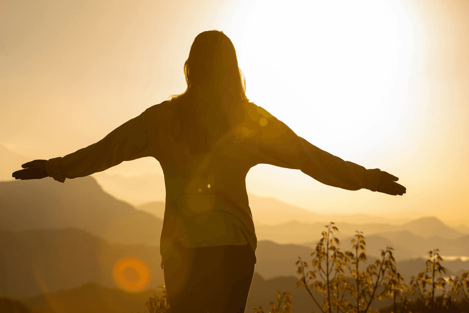 Person standing on a hilltop at sunrise with arms open, looking toward the horizon
