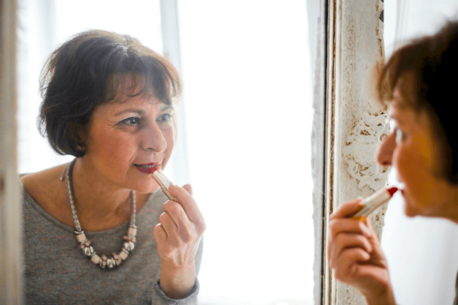 Person looking into a mirror with warm golden light, expression of self-recognition and compassion, representing mirror work practice