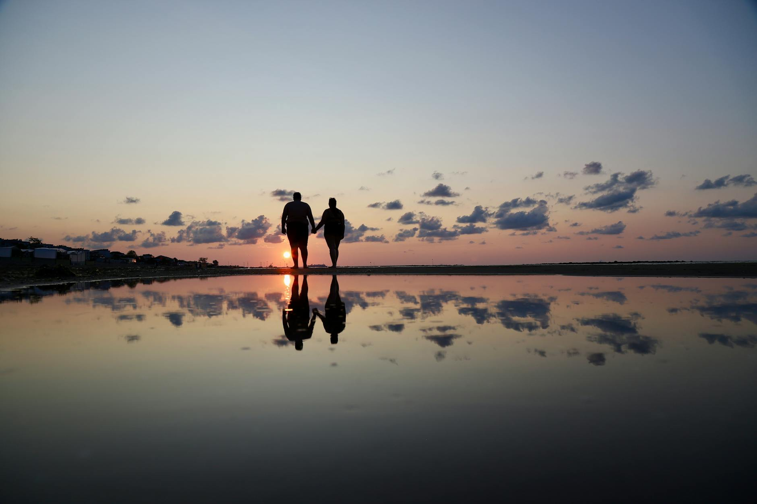 Two silhouettes walking together toward a sunset on a peaceful beach